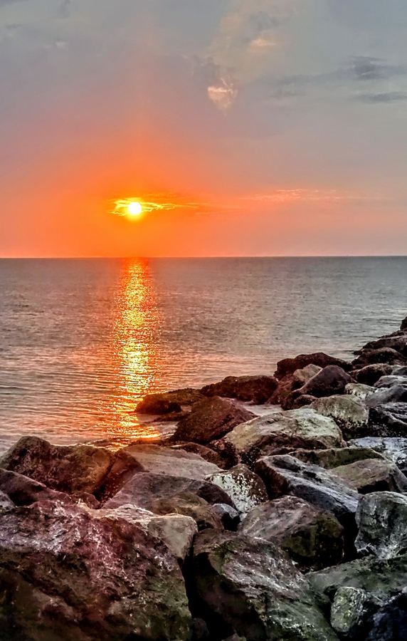 Sun setting over calm water beyond a rocky jetty